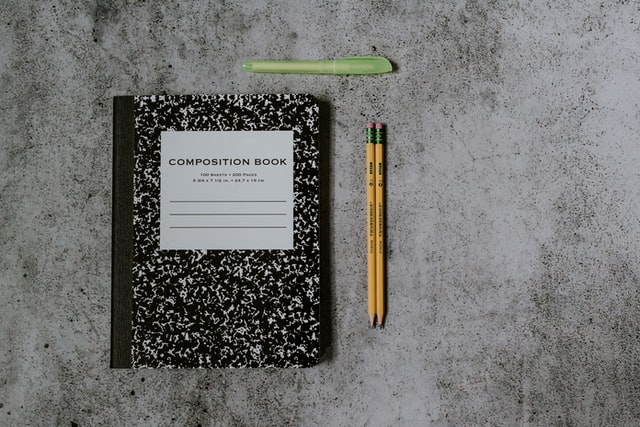 caderno preto e em volta lápis e caneta